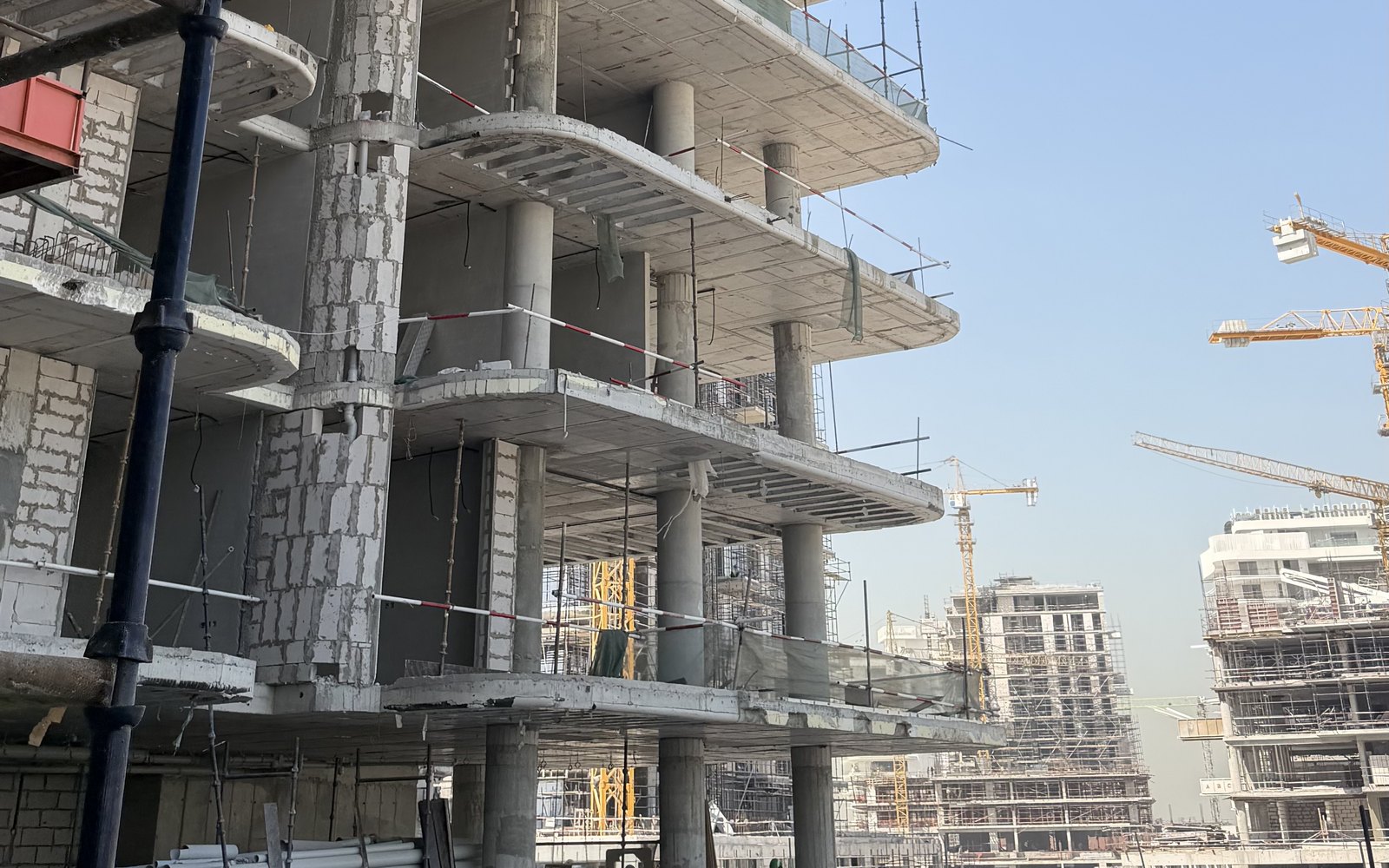 Residential building under construction in Dubai with curved balconies, with tower cranes and more towers being built behind